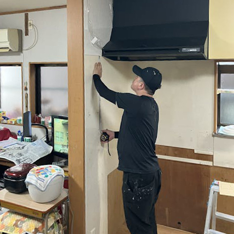 レンジフードをよけた形にキッチンパネルを加工するため、慎重に寸法を測っています。