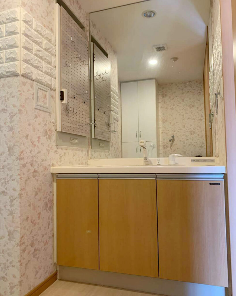 ピンクの小花柄の壁紙で、可愛らしいイメージの洗面所。<br />
今回は洗面化粧台は残し、内装のみリフォームします。