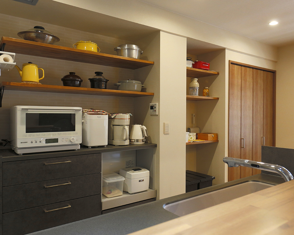 「魅せる」と「使う」を両立した背面収納は、キッチン本体とおそろいのデザインで統一感を演出。
上部にはオープンな飾り棚を造作しました 。
奥様お気に入りの調理道具や鍋を並べて、使うたびに気分が上がる「見せる収納」を楽しめます 。