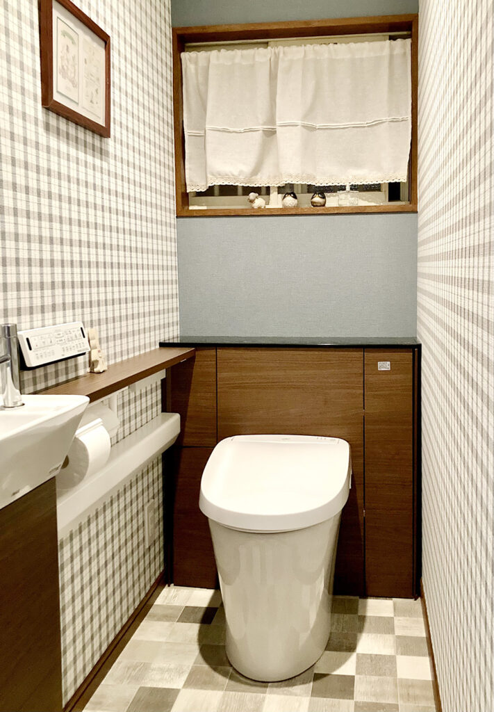 LIXILリフォレは背面のキャビネットまでセットのトイレ。<br />
T様がセレクトされたのは、トイレ横の手洗いカウンターもセットの商品です。<br />
給水管やコードはキャビネット内に隠し、お掃除道具やトイレットペーパーも収納できてトイレがスッキリ使えます。<br />
内装はかわいいチェック柄にブルーグレーの壁紙を合わせました。<br />
窓枠の色とトイレキャビネットの色を揃え、空間のアクセントになっています。