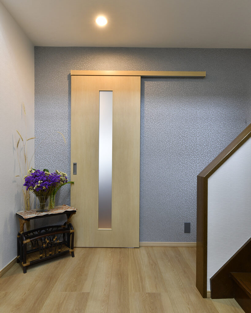 玄関ホール、正面にはエレガントなブルーのアクセントクロスを貼りました。<br />
ダウンライトが優しく室内を照らします。